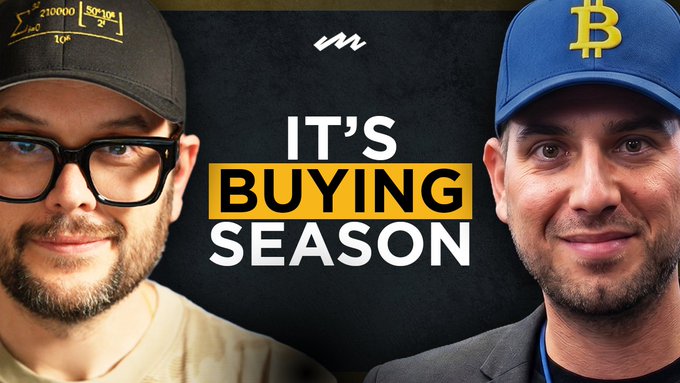 Thumbnail-style image featuring two men (one in a black cap with glasses, one in a blue Bitcoin cap) alongside the text "IT'S BUYING SEASON" in yellow and white.