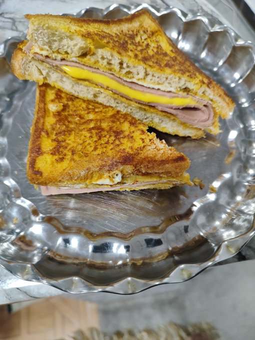 A grilled ham and cheese sandwich cut diagonally into two triangles, served on a scalloped silver platter.