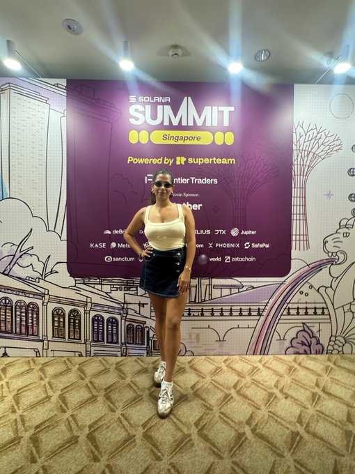 A woman poses confidently in front of the purple "Solana Summit Singapore" backdrop, powered by Superteam, featuring sponsor logos like Jupiter, Jito, Phantom, and SafePal. The image captures the energetic, community-driven spirit of her post, serving as a visual "GM" greeting from the event while inviting others to connect.