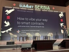 A speaker delivers a presentation on stage at the Solana Summit Serbia event, with a large screen behind them displaying the talk title "How to vibe your way to smart contracts" by Nick Hernandez. The setup, featuring modern chairs and a clean stage design, matches the post's reference to the speaker's talk about simplifying smart contract development with AI agents.