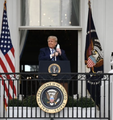 A man stands at a podium bearing the Presidential Seal of the United States, flanked by American flags on what appears to be the White House balcony or entrance.