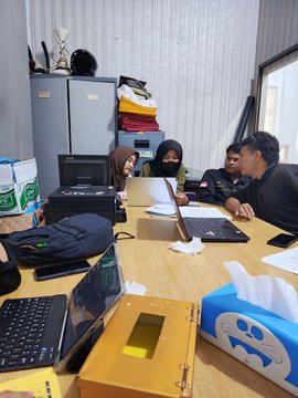 In this image, a group of people are gathered around a table with laptops, possibly discussing financial matters. This scene could represent the "thorough" research Sari's husband may have done before quitting his job to trade crypto, or it could depict a team meeting to analyze market trends.