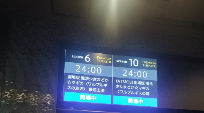 A cinema display board showing Screen 6 and Screen 10 'Premium Theater' showings at 24:00 for '劇場版 魔法少女まどか☆マギカ 〈ワルプルギスの廻天〉', with 開場中 (now showing) status.
