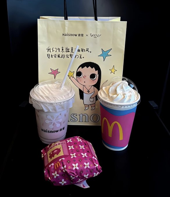 A McDonald's meal featuring two drinks—a Naisnow milkshake and a McDonald's sundae—along with a wrapped burger and a branded paper bag displaying a cartoon girl and Chinese text.