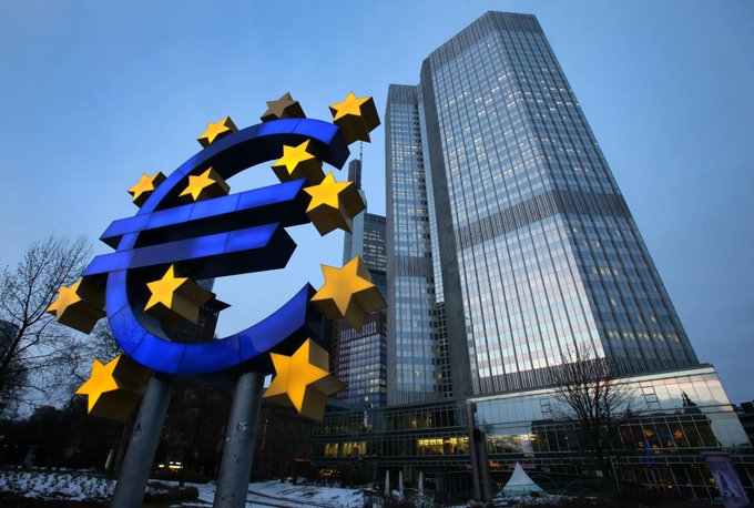 The iconic blue Euro sign sculpture with yellow stars stands in front of the European Central Bank skyscraper in Frankfurt.
