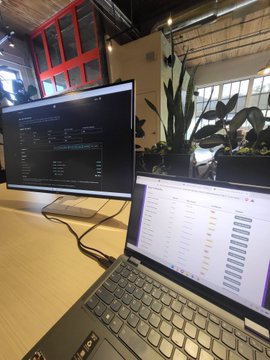 A dual-monitor workspace setup with an external monitor and laptop displaying data screens on a wooden table.