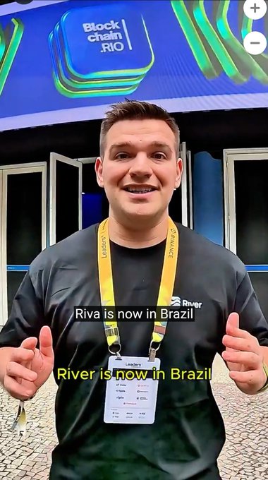 A photo of a smiling man wearing a "Leader" badge at an event, with text overlay reading "Riva is now in Brazil" and "River is now in Brazil," with "Blockchain Rio" signage behind him.