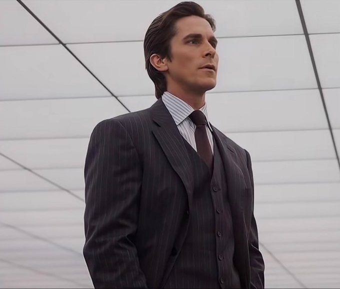 A man in a sharp pinstripe three-piece suit with a striped shirt and burgundy tie stands confidently in a modern, minimalist white room with a geometric ceiling. His poised, upward gaze mirrors the triumphant "feeling when you move SL to BE," capturing the swagger of a successful strategic play.