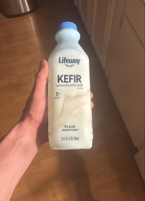 A hand holds up a 32 fl oz bottle of Lifeway Plain Unsweetened Lowfat Kefir (1% milkfat), with the caption "Banging." suggesting the drink is delicious.