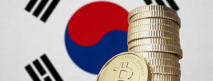 Stacked gold Bitcoin coins stand prominently in the foreground against the backdrop of the South Korean flag, symbolizing the surge in crypto trading volumes on platforms like Upbit as investors pivot away from the declining KOSPI stock market toward digital assets.