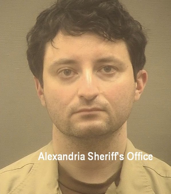 A mugshot from the Alexandria Sheriff's Office showing a dark-haired man in a tan shirt against a gray background.