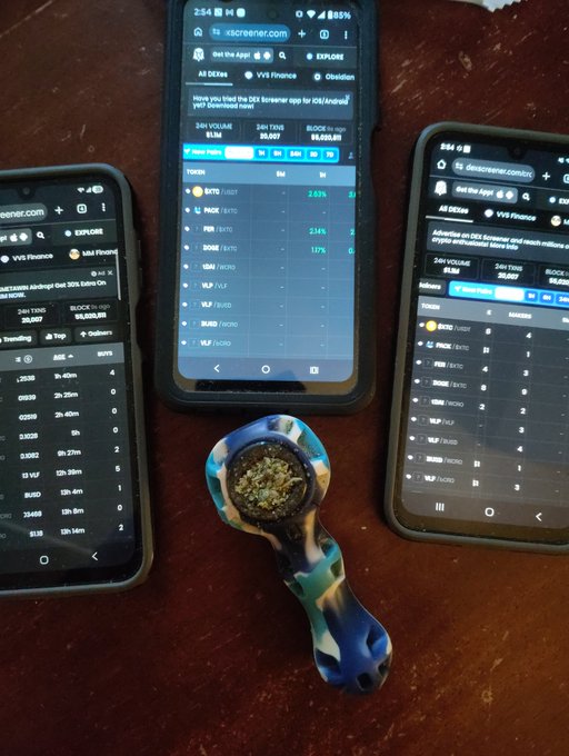 Three smartphones displaying the xscreener.com finance app showing stock and crypto tickers including BTC, IBIT, FGN, DOW, VTI, and VLP, alongside a colorful glass pipe on a dark wooden surface.
