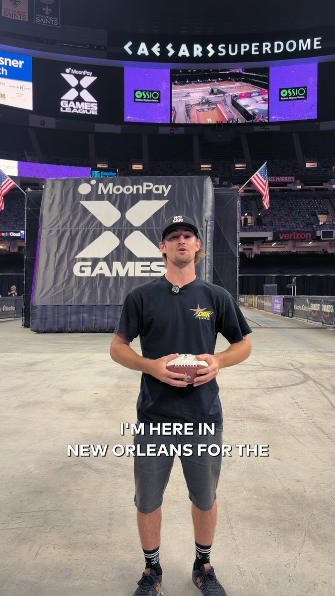 A man holding a football stands at the Caesar's Superdome in New Orleans, with "MoonPay X Games" branding on a large screen behind him, announcing the start of Day 2 of the X Games League Championship.