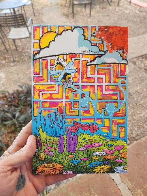 A hand holds a colorful mixed-media artwork featuring a cartoon bee, a maze-patterned sky with sun and clouds, and a vibrant garden of flowers, with the text 'breaking thesaame' visible.