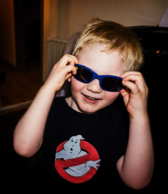 A young blonde-haired boy wearing blue sunglasses and a Ghostbusters t-shirt grins at the camera, playfully holding the sunglasses to his face.

The post mentions reaching out to a project and becoming their ambassador, but the image itself doesn't appear to directly relate to that message—instead showing a casual, fun moment of a child enjoying wearing sunglasses.