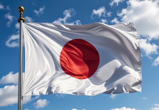 The image shows the flag of Japan waving against a blue sky with white clouds, symbolizing the country where SBI Group's $250 billion partnership with Ondo Finance will bring Japanese stocks on-chain and facilitate tokenized asset settlements using SBI's yen stablecoin.