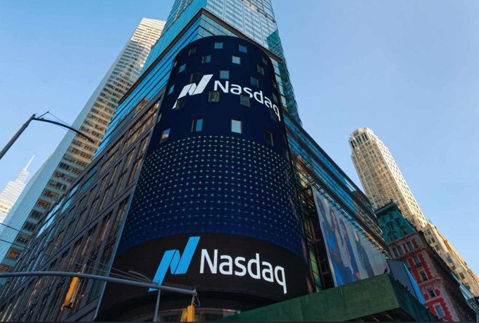 A low-angle photograph of the Nasdaq building in Times Square, New York, displaying its iconic blue digital screens with the 'Nasdaq' logo prominently featured.