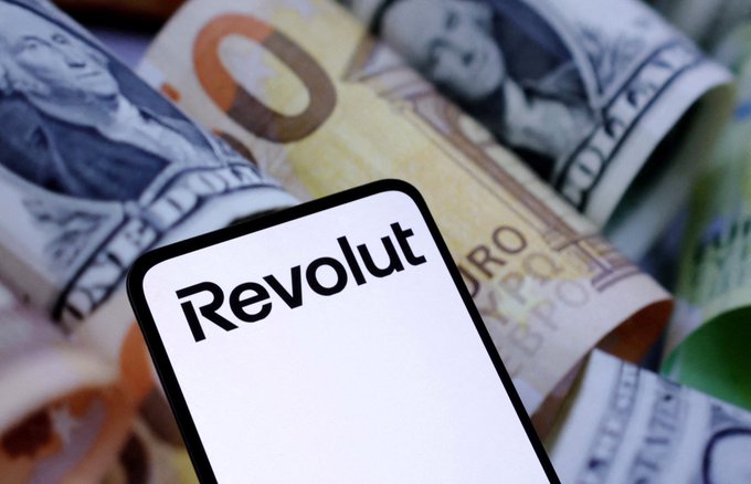 A smartphone displaying the 'Revolut' logo rests on top of a pile of Euro and US Dollar banknotes.