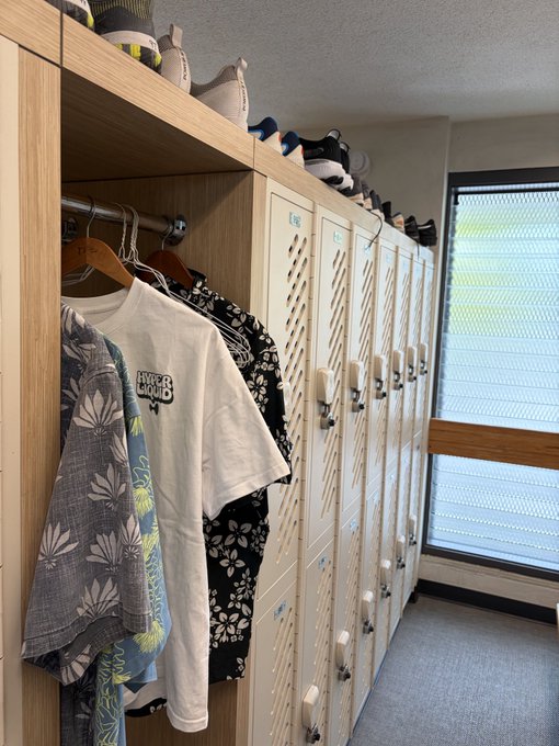 A white t-shirt with "HYPER LIQUID" printed on it hangs in a locker next to other clothing, with shoes neatly lined up on top of the lockers. This directly relates to the post's mention of "hyperliquid" by showcasing the brand's apparel.