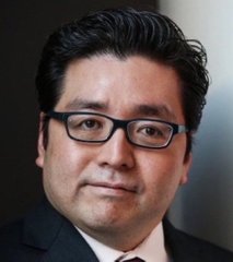 A headshot image of Tom Lee, a man with dark hair wearing black-rimmed glasses and a dark suit with a white shirt and tie, posed against a blurred backdrop. The photo accompanies breaking news of his company BitMine acquiring 15,112 ETH valued at $41 million, identifying him as the figure behind the significant crypto purchase.