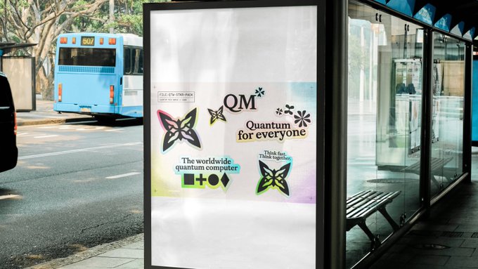 An outdoor advertisement at a bus stop promotes a quantum computer with colorful graphics and text reading 'QM Quantum for everyone' and 'The worldwide quantum computer,' while a blue city bus passes by in the background.