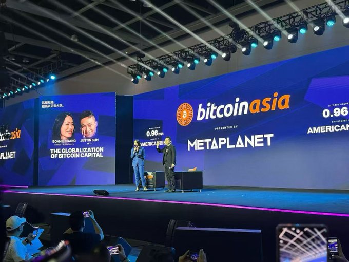 The image shows Ronnie Cheng and Justin Sun presenting on stage at the Bitcoin Asia conference, sponsored by Metaplanet, featuring a promotional banner titled "The Globalization of Bitcoin Capital" with a countdown timer showing "0.96 DAYS SPONSORED BY AMERICAN [Express]." This relates to the post's discussion about the Hong Kong Bitcoin conference, highlighting the speaker lineup—likely including Justin Sun ("孙哥"), whose presence the post mentions being a notable talking point amid otherwise lackluster event coverage.