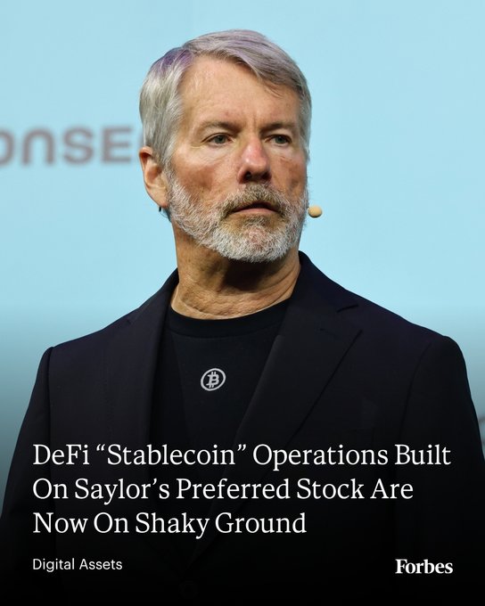 Michael Saylor, wearing a black blazer and a headset microphone, speaks at a podium with the article headline "DeFi 'Stablecoin' Operations Built On Saylor's Preferred Stock Are Now On Shaky Ground" displayed below—visually anchoring the Forbes Digital Assets piece about how DeFi stablecoins tied to Strategy's preferred stock are facing instability amid Bitcoin's downturn.