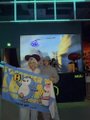 A small pixelated image showing a person in a hat holding a yellow flag or banner in what appears to be a dimly lit room or venue.