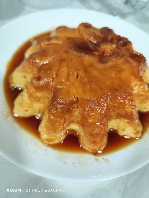 A dessert shaped like a maple leaf is drizzled with caramel sauce and served on a white plate.