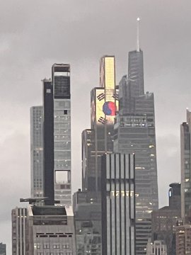 A cityscape view of tall skyscrapers, with one building displaying a large graphic of a hand holding a red heart on its facade under a cloudy sky.