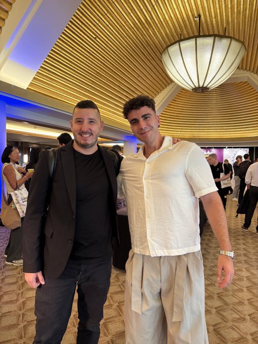 Two men smile for a photo in an elegant venue with a striking ribbed wooden ceiling and ornate pendant light, capturing an in-person meeting at the Solana Summit between a CT creator and notable crypto personality @StarPlatinum_.