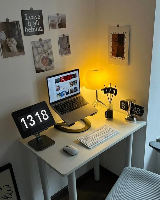 A desk setup featuring a laptop, a yellow lamp, and a tablet displaying '1318', with various photos and art prints pinned to the wall, including one reading 'Leave it all behind.'
