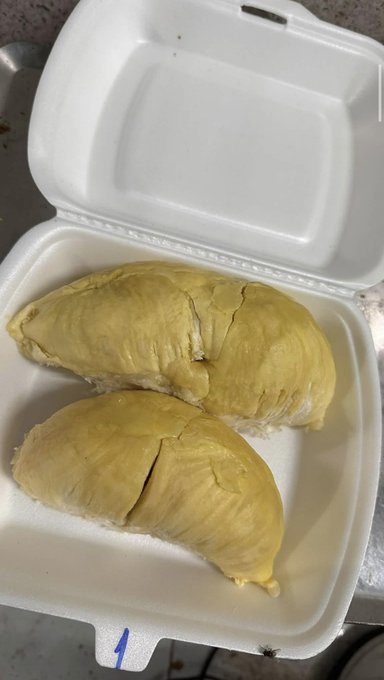An open styrofoam takeout container holding two pieces of yellow, fleshy food, likely durian fruit.