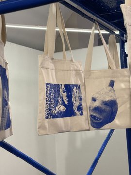 Canvas tote bags with blue printed designs hanging on a blue metal rack.