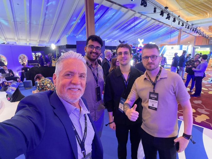 Four men smile for a selfie at a conference, with one wearing a 'CREATIVE' lanyard and 'MINI LAUREATE' badge.
