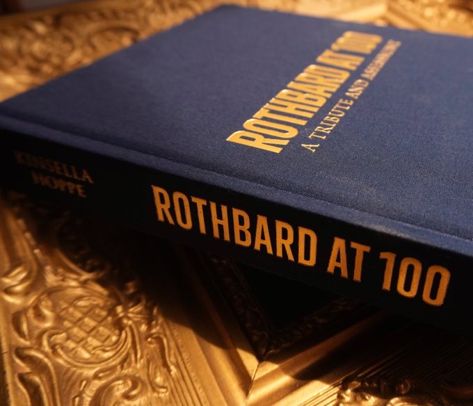 A hardcover book titled 'Rothbard at 100: A Tribute and Assessment' by Kensella and Hoppe, resting on an ornate gold surface.