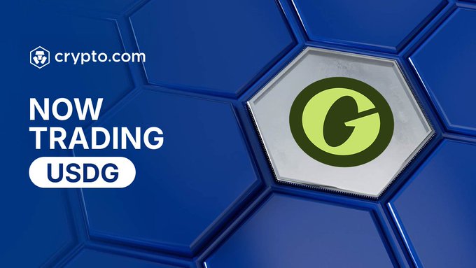 Crypto.com promotional graphic with a blue hexagonal background featuring the Crypto.com logo and the text "NOW TRADING USDG," alongside a metallic hexagonal token displaying the green Global Dollar (USDG) logo, announcing USDG's availability for trading in the Crypto.com App as described in the post.