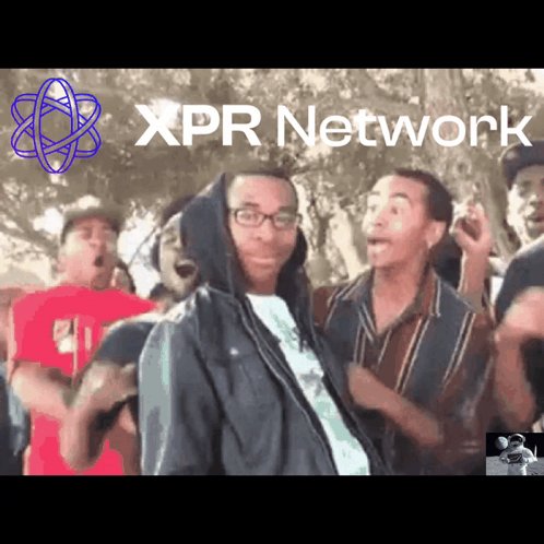 The image features a group of people standing together, with one man wearing glasses and holding a microphone. The background includes trees and a banner that says "XPR Network" written in purple letters.