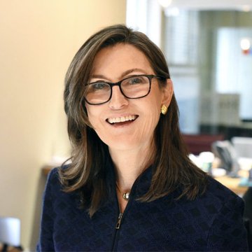 The image shows a smiling woman with shoulder-length brown hair, glasses, and a dark navy blazer, likely a corporate portrait of a business executive. This appears to be Cathie Wood, CEO of ARK Invest, whose firm just announced a $37 million purchase of Bitcoin ($BTC), connecting the portrait to the breaking news about her company's latest crypto investment.