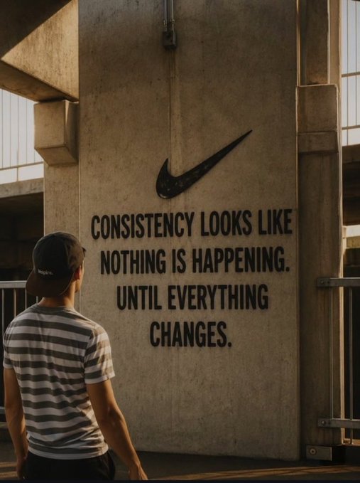A man in a striped shirt and cap stands looking at a large concrete wall featuring the Nike swoosh logo and the motivational quote 'CONSISTENCY LOOKS LIKE NOTHING IS HAPPENING. UNTIL EVERYTHING CHANGES.'