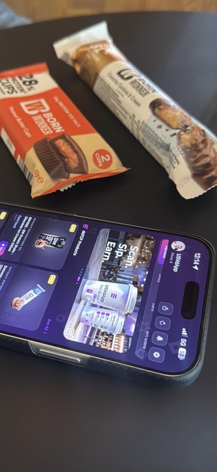 Two protein bars rest on a dark table next to a smartphone displaying a barcode scanning app interface.