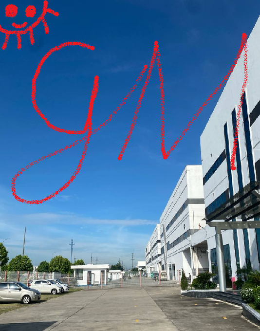 A bright blue sky above an industrial or commercial building complex, marked with red digital scribbles resembling 'GM' and a small stick figure drawing in the upper left corner.