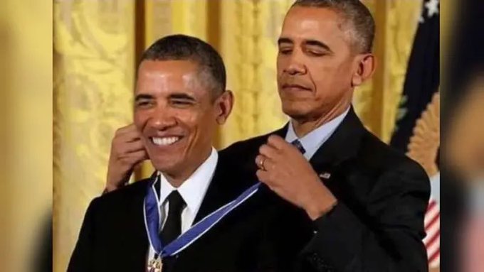 Former President Barack Obama smiles as another man places a medal with a blue and white ribbon around his neck in an official ceremony.