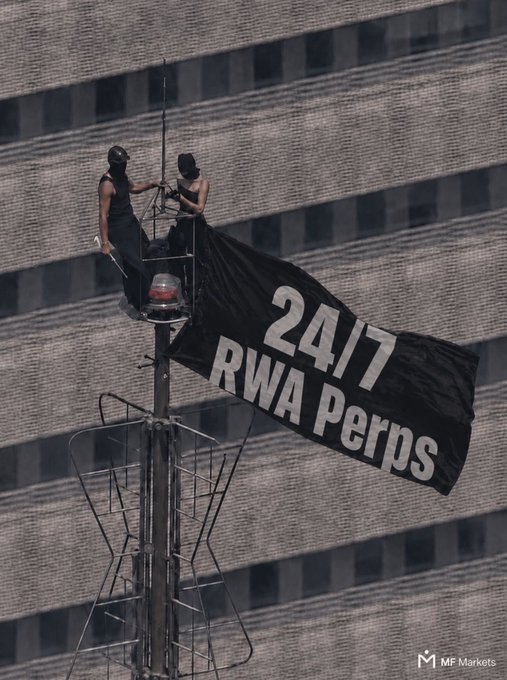 Two masked individuals stand atop a tower spire, having unfurled a black banner reading "24/7 RWA Perps" against a backdrop of a building's facade, evoking the headline's imagery of a daring activist statement from an extreme heights stunt.