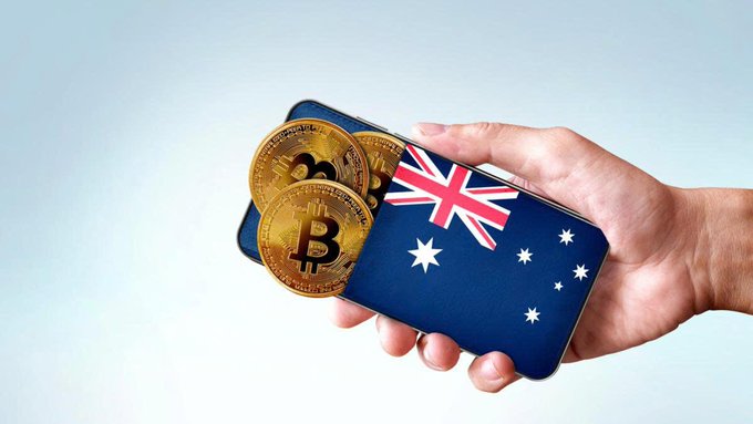 A hand holds an Australian flag alongside physical Bitcoin coins, symbolizing Australia's regulatory approach to digital asset companies, which ASIC has imposed a licensing deadline on by September 30, 2026, with penalties up to 10% of revenue for non-compliance.