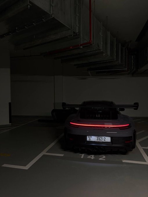 Rear view of a Porsche 911 GT3 parked in a dimly lit underground garage spot numbered 142, featuring a distinctive red LED light bar and Dubai license plate 35212.