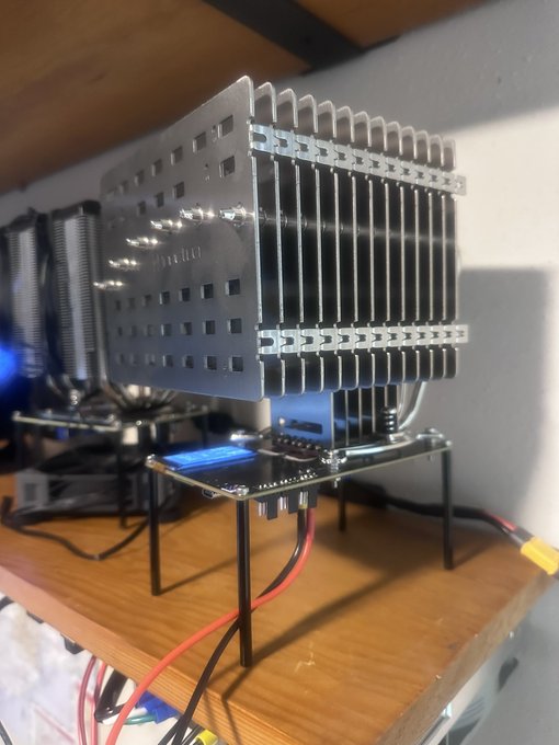 A close-up shows a computer CPU cooler with a large silver finned heatsink mounted on a motherboard, illuminated by blue LED lighting on a wooden desk.