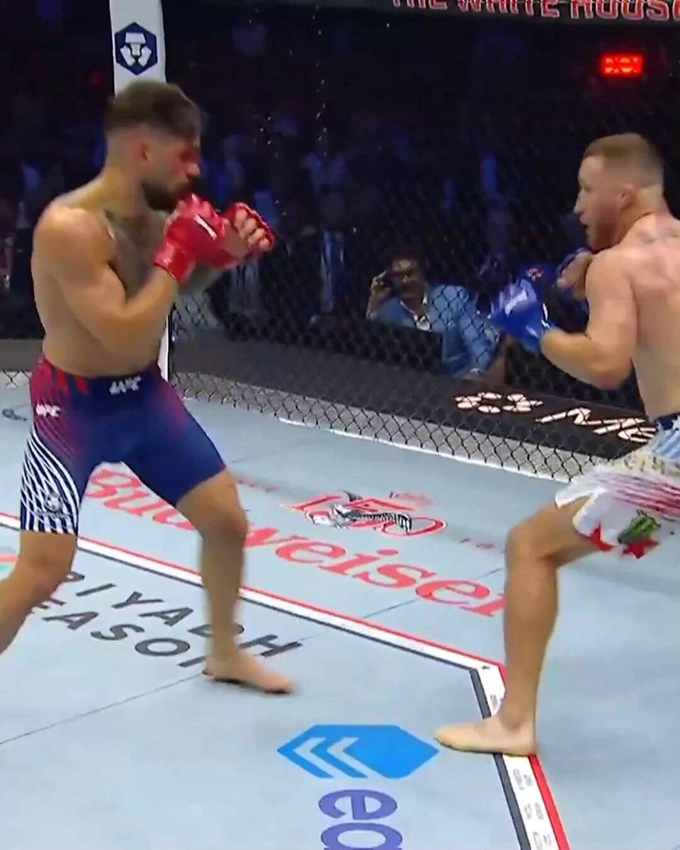 The image shows two men fighting each other, with one man wearing a red glove and the other wearing blue gloves. The fighters are both barefoot, which adds to the intensity of their match. The scene takes place inside a ring or arena, as indicated by the presence of a fence in the background. The post accompanying the image is titled "GETTING STARTED EARLY @Justin_Gaethje | Live Now on @ParamountPlus [ Title fights presented by @Cryptocom ]". This suggests that there might be an upcoming event related to fighting or combat sports, possibly involving these two men as participants.