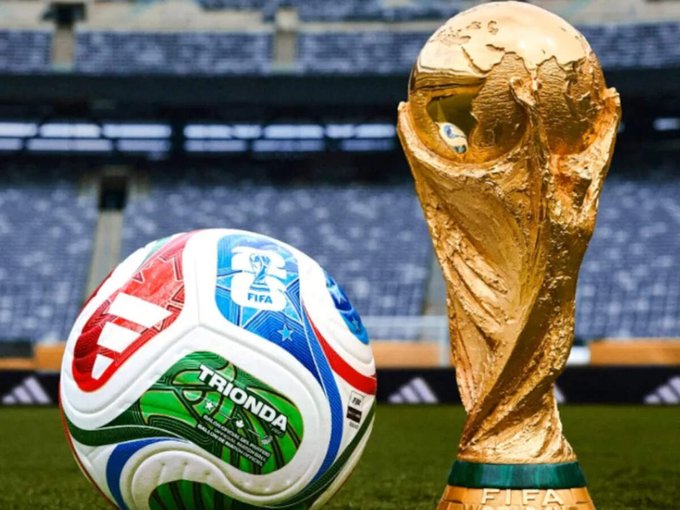 The image features a soccer ball and a trophy for the FIFA World Cup. The soccer ball has a green, white, red, and blue design, while the trophy is gold with a black base. Both objects are placed on a field of grass. In the background, there's an empty stadium filled with seats, suggesting that this scene takes place during or after a major soccer event like the World Cup. The image also includes text about a prediction market called @Polymarket and a platform named @ Chance.