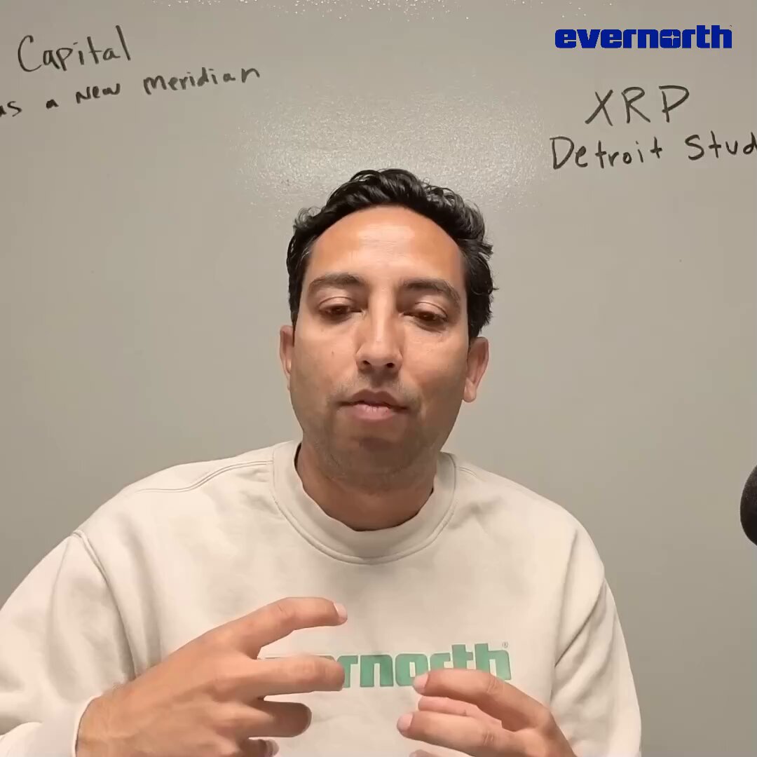 The image shows a man wearing a white sweatshirt with green text, talking about tokenization. The man has his hands up, emphasizing his point as he speaks. The background of the image features a whiteboard with writing on it, which includes words like "Capital", "Meridian", and "XRP". There is also an image of a person's hand holding a pen in the bottom right corner of the photo.